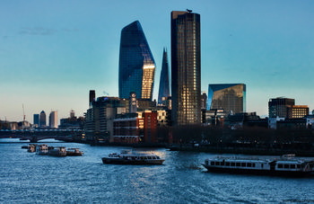 Thames skyscrapers This urban architecture photograph captures the skyscrapers along the River Thames in London, United Kingdom, during an evening in winter. The image features prominent landmarks such as 30 St Mary Axe, commonly known as the Gherkin, as well as 122 Leadenhall Street, often referred to as the Cheese Grater. Several boats are visible on the river, emphasizing the activity on the Thames against the backdrop of London's skyline. The evening light highlights the glass facades of these modern buildings, showcasing the architectural styles found in this part of the city.
